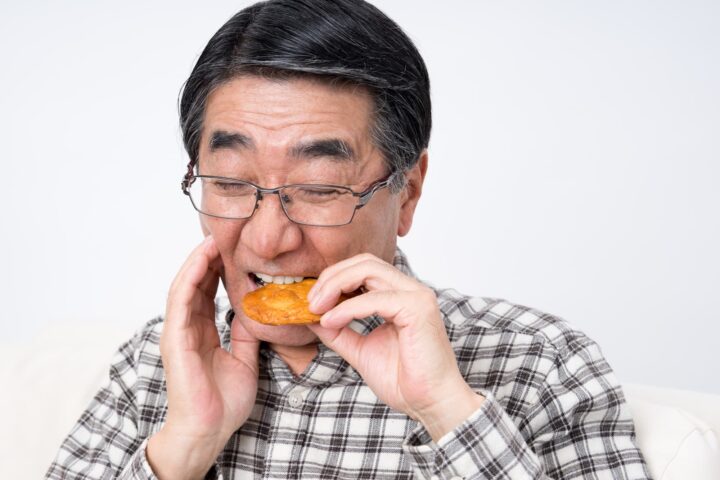 顎を押さえながらせんべいをかじる男性