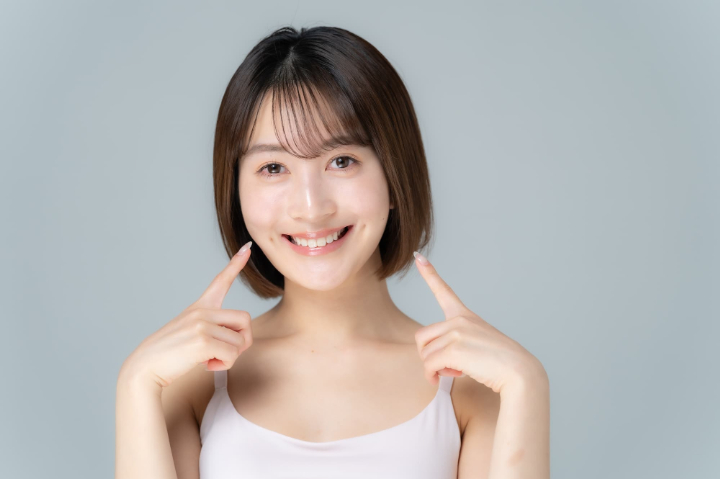 両手の人差し指で自分の口元を指さす笑顔の女性