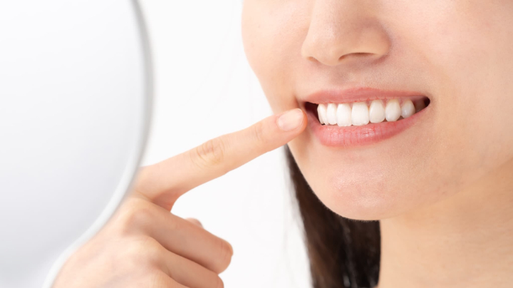 セラミックできれいになった前歯を鏡で見て満足そうに微笑む女性